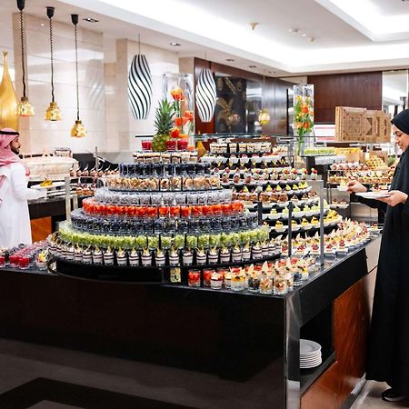 Swissotel Makkah Mecca Exterior photo The photo shows a luxurious buffet setup in a dining area. There is a prominent display of desserts arranged in a visually appealing manner, featuring various small containers filled with colorful treats, including fruit, creams, and pastries. A woma