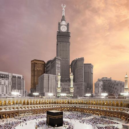 Swissotel Makkah Mecca Exterior photo The photo depicts the iconic Kaaba, located in Mecca, Saudi Arabia, surrounded by a large congregation of people performing the Hajj pilgrimage. In the background, there is a prominent clock tower building, which is part of the Abraj Al Bait complex.