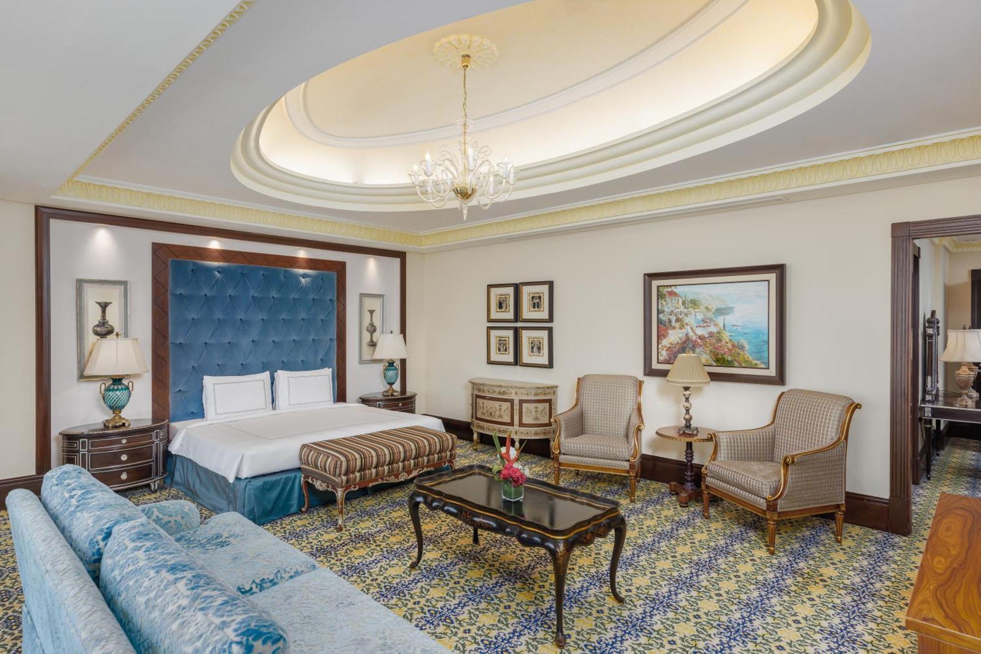 Swissotel Makkah Mecca Exterior photo The photo shows a luxurious hotel room featuring a spacious layout. In the center, there is a well-made bed with a padded blue headboard. A decorative patterned rug covers the floor. To the side, a comfortable, light blue sofa is positioned, accompan