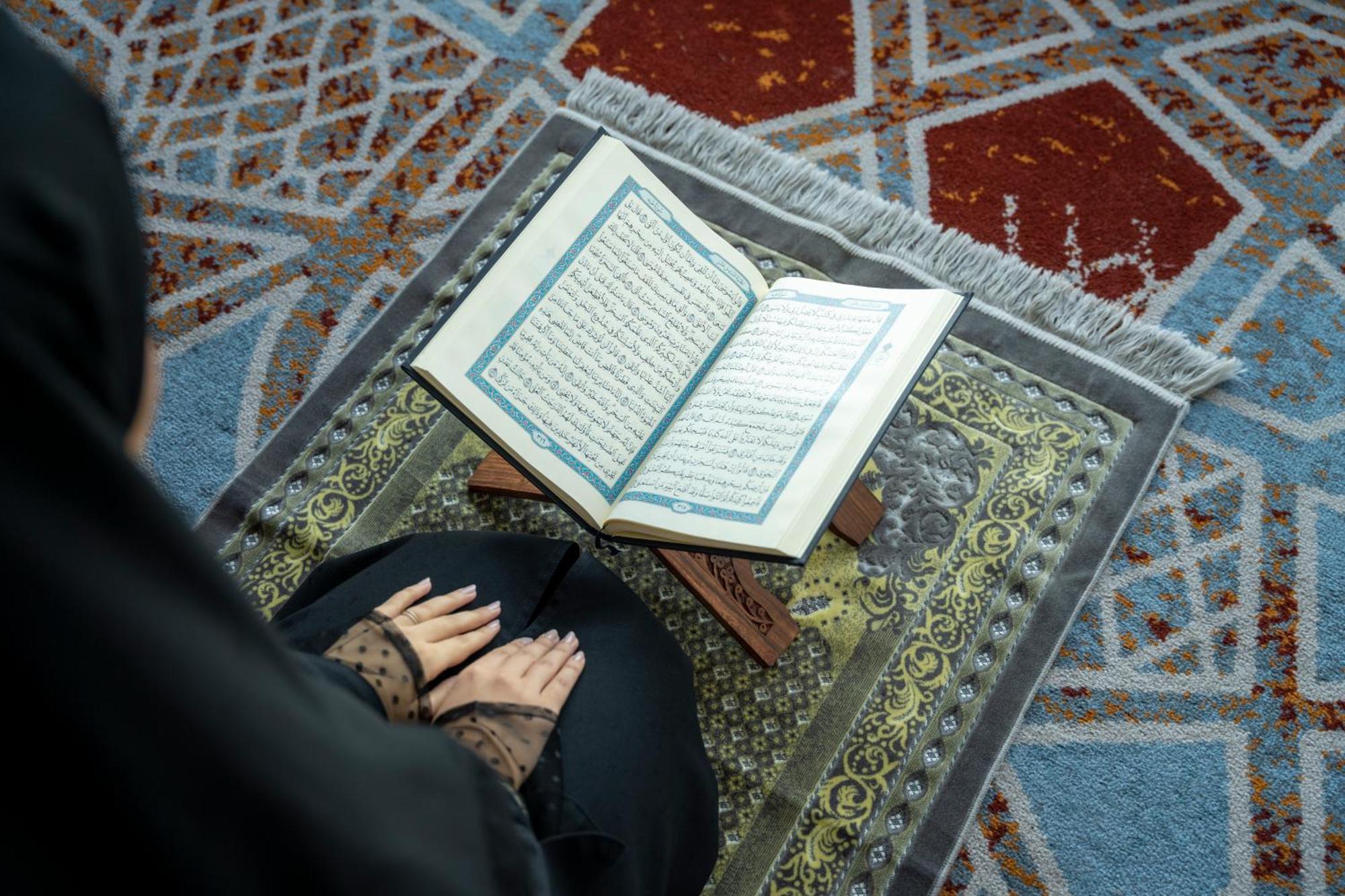 Swissotel Makkah Mecca Exterior photo The photo shows an individual, likely sitting on a prayer mat, with their hands placed on or near an open Quran. The Quran is displayed on a wooden stand, and the prayer mat features intricate patterns. The setting suggests a moment of prayer or refl