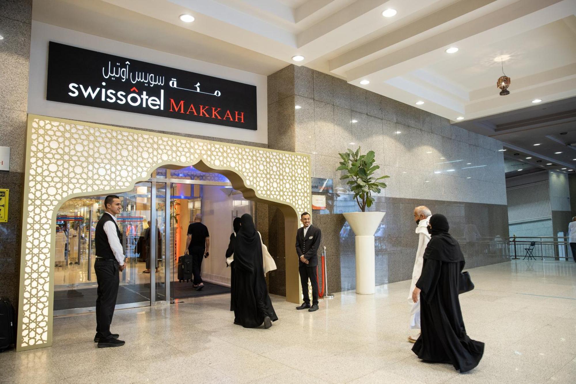 Swissotel Makkah Mecca Exterior photo The photo shows the entrance of the Swissotel, located in Makkah. The entrance features an ornate archway with decorative designs. There are several people visible, including staff members in formal attire and guests. The staff are standing attentive