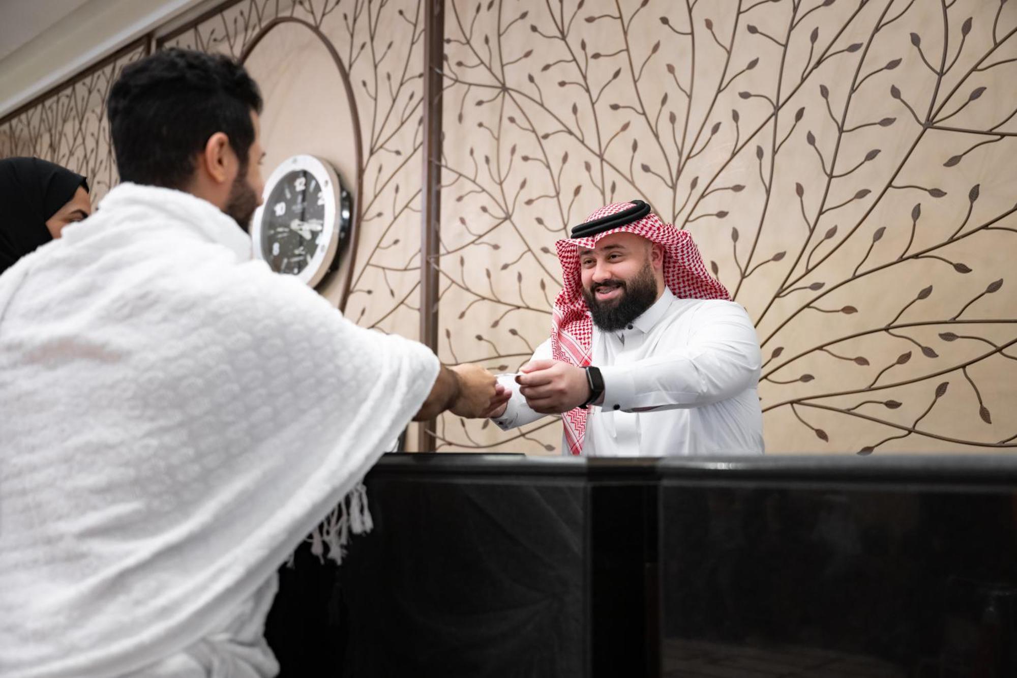 Swissotel Makkah Mecca Exterior photo The image shows two men interacting in a welcoming setting, likely indicative of a hospitality environment, such as a hotel or reception area. One man is dressed in white traditional attire, possibly indicating he is performing a pilgrimage. The othe