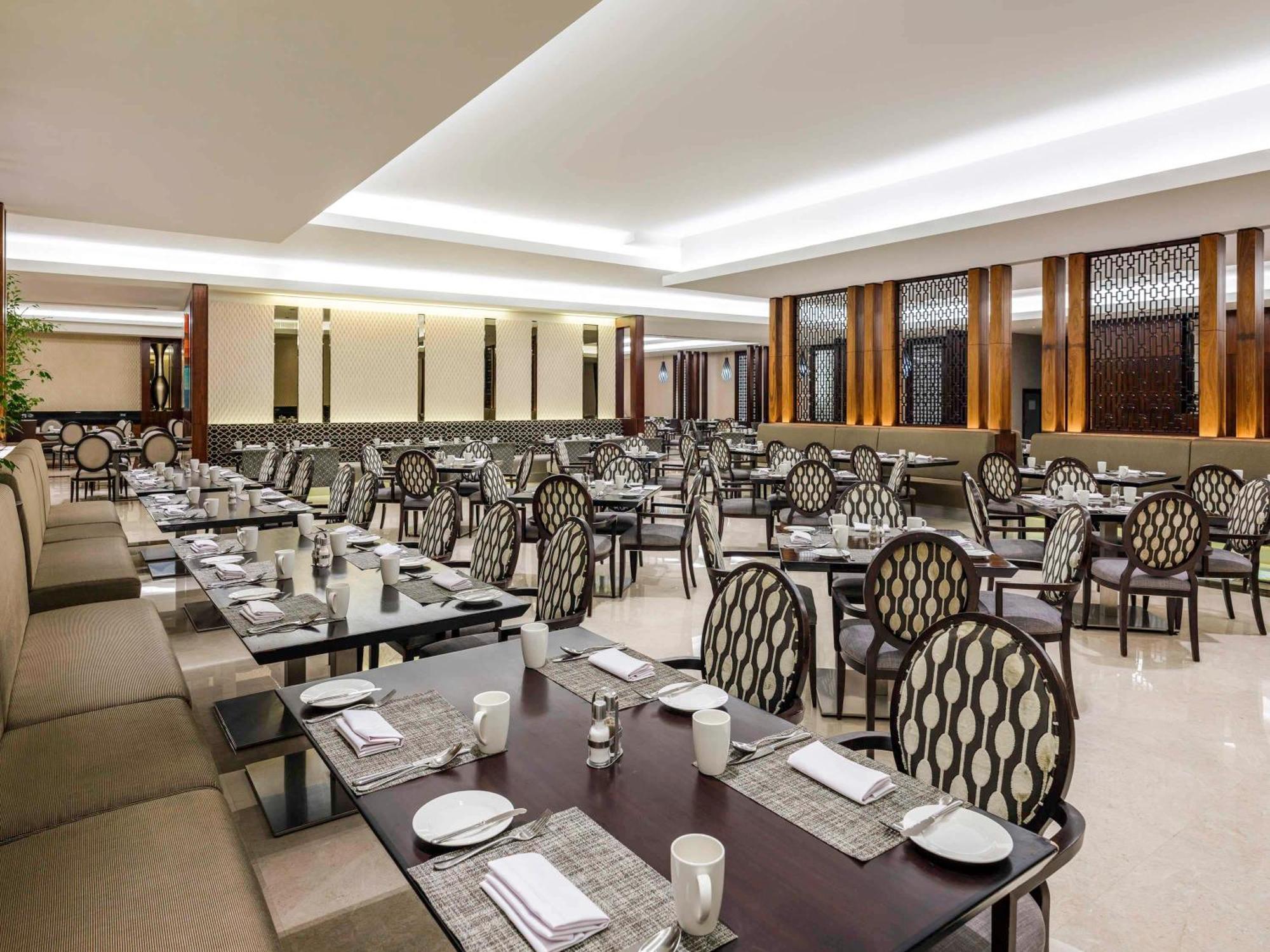 Swissotel Makkah Mecca Exterior photo The photo shows the interior of a restaurant. It features a spacious dining area with rows of tables and elegant chairs. The tables are set with white plates, cups, and utensils, indicating that they are ready for guests. The decor includes light-col