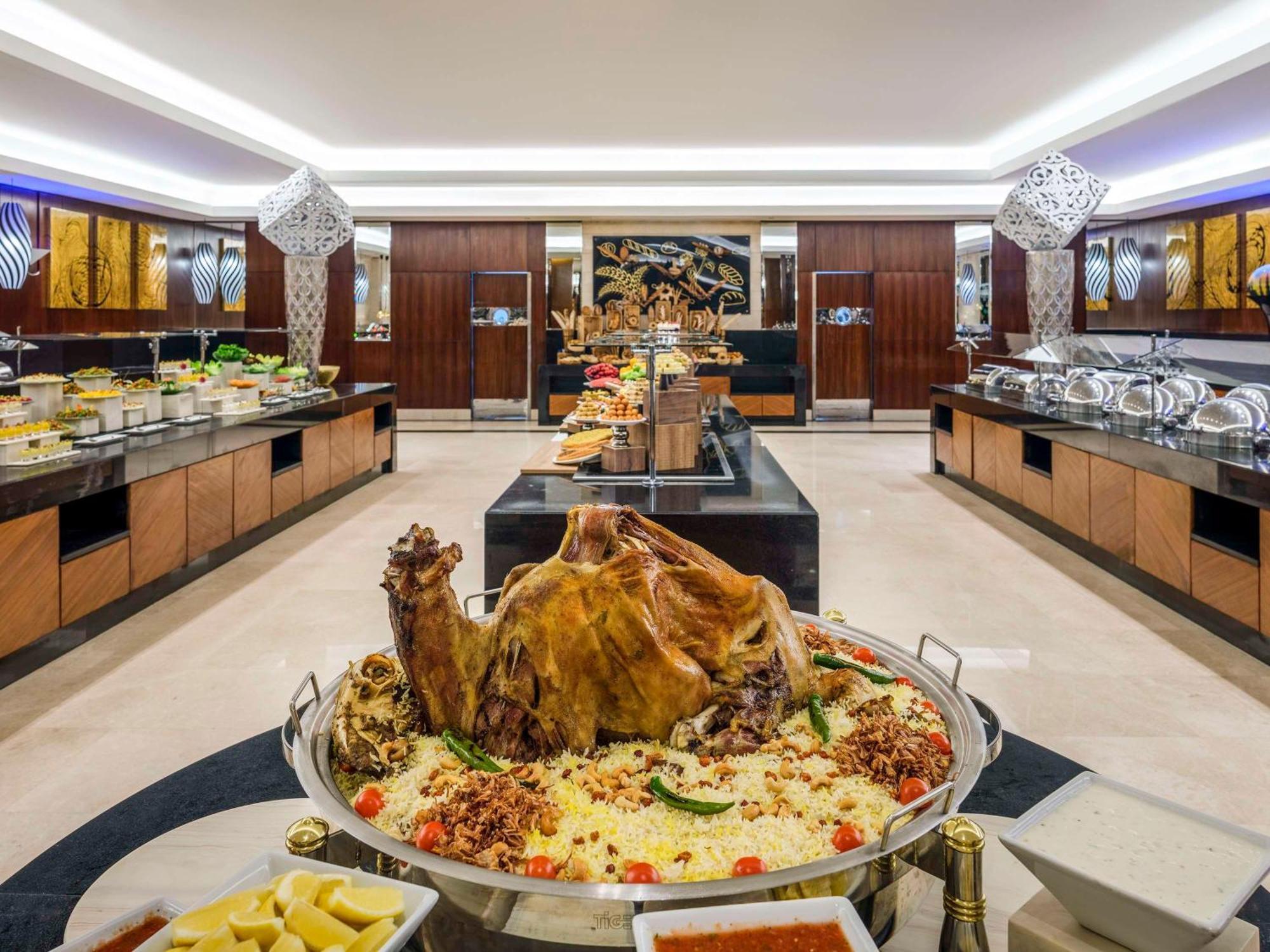 Swissotel Makkah Mecca Exterior photo The photo shows a lavish buffet setup in a restaurant or banquet hall. In the center, there is a large display of a roasted whole lamb or goat, garnished with herbs and served on a platter with rice and colorful accompaniments. Surrounding this cente