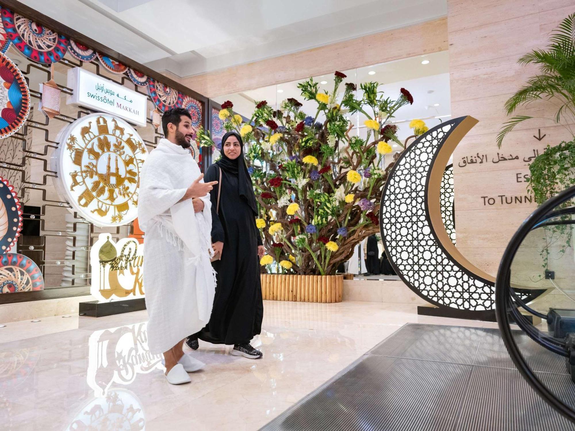 Swissotel Makkah Mecca Exterior photo The photo shows a modern, spacious interior, likely of a shopping mall or a public space. Two individuals are walking together; one is wearing a traditional white garment, while the other is dressed in a black abaya. In the background, there are deco